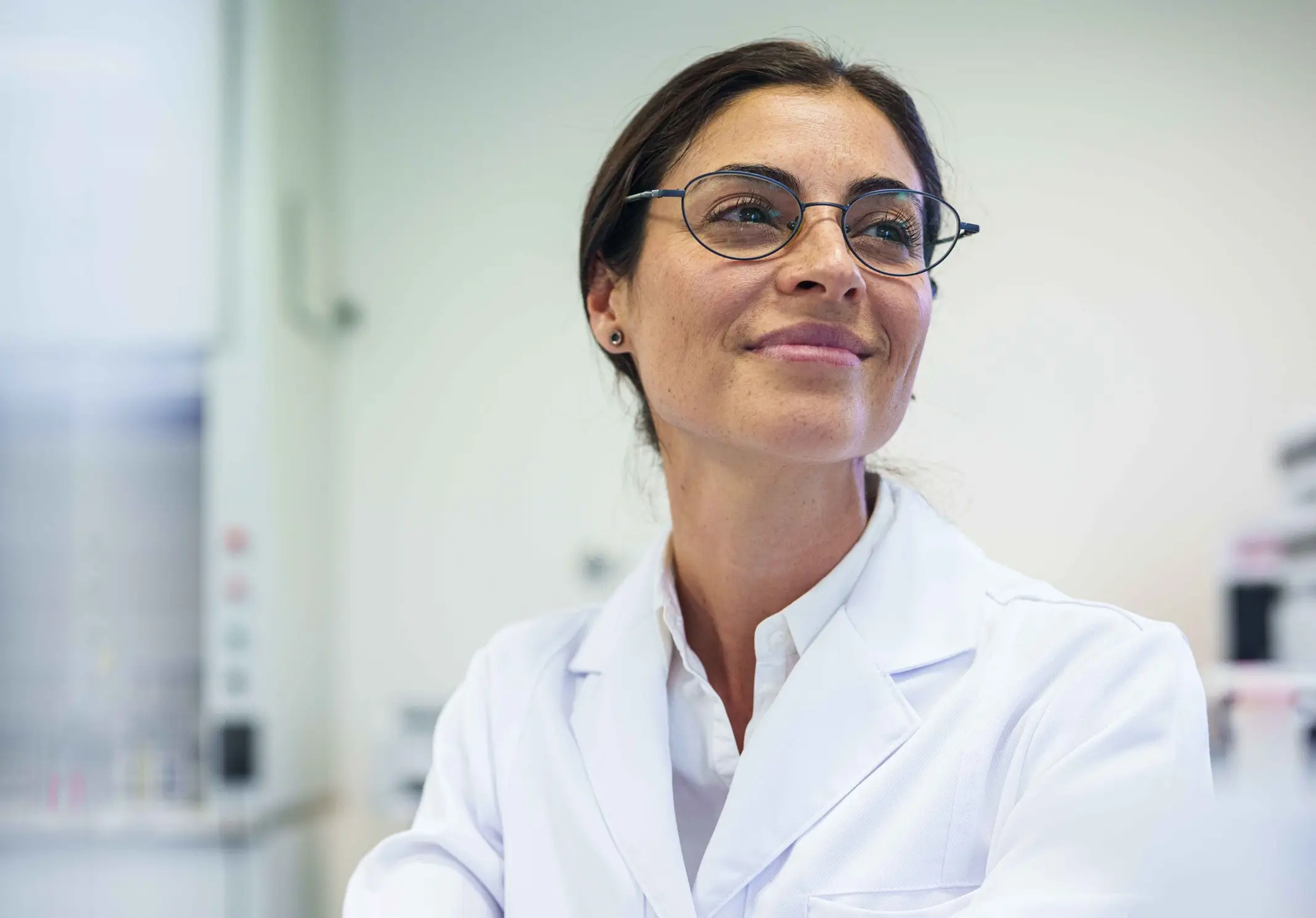 A smiling female scientist in a white lab coat and glasses