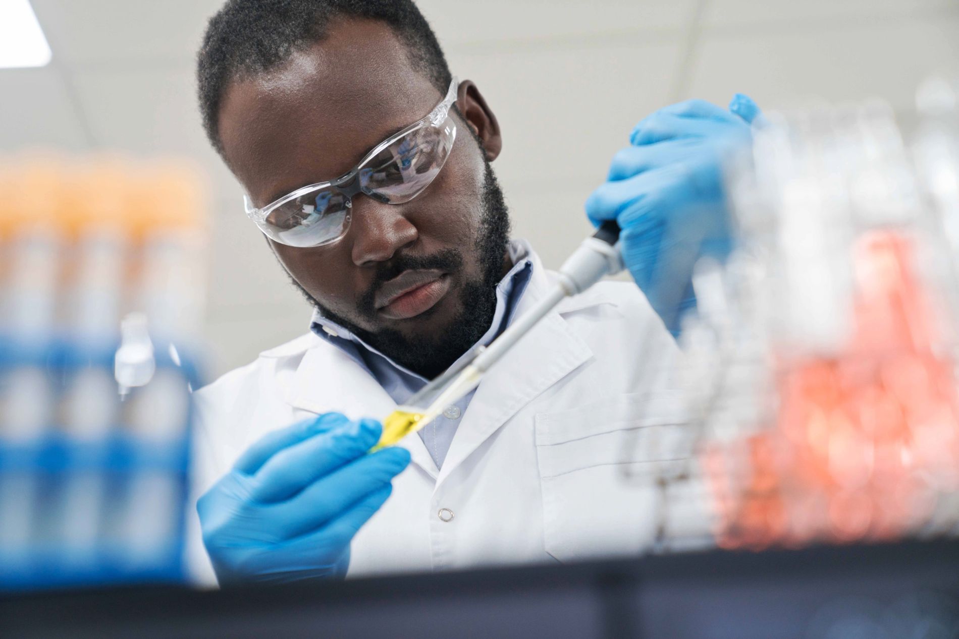 A scientist carefully uses a pipette to transfer yellow liquid between tubes in a lab.