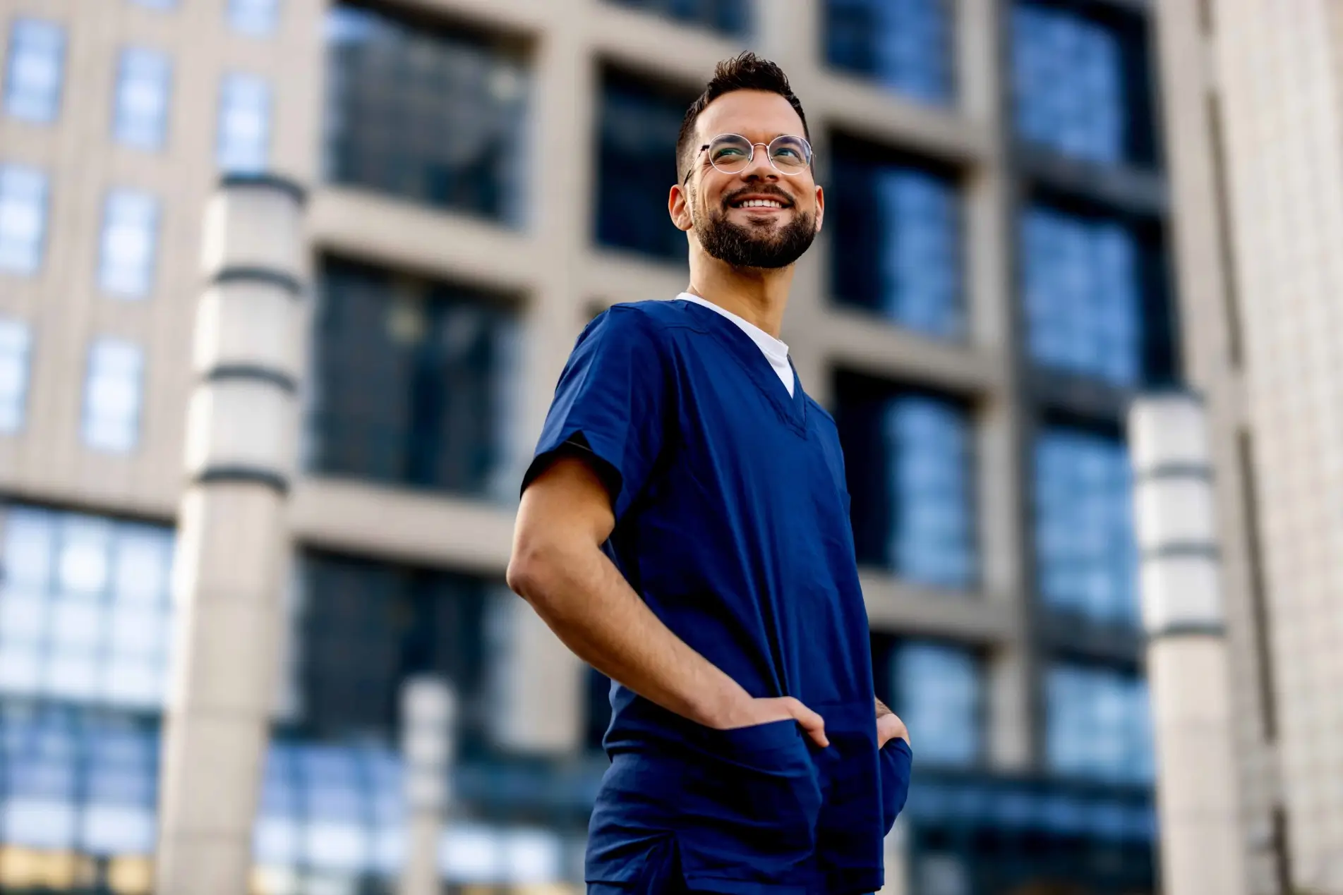 Un hombre feliz con uniforme azul y gafas de pie fuera de un edificio.